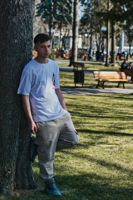 a young man poses against a tree in the park