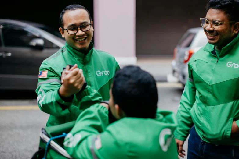 three men in green shirts and black pants, one pointing to another