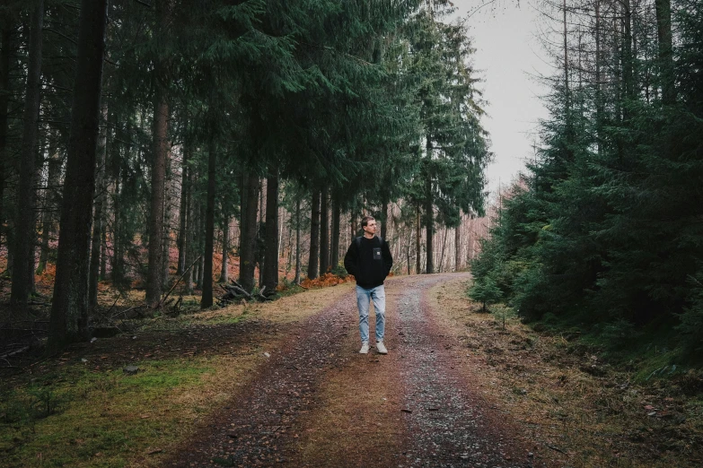 man standing in the middle of a road surrounded by trees