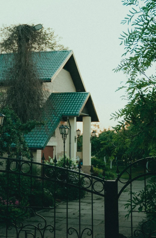 a house behind a black fence with a green roof and a light on