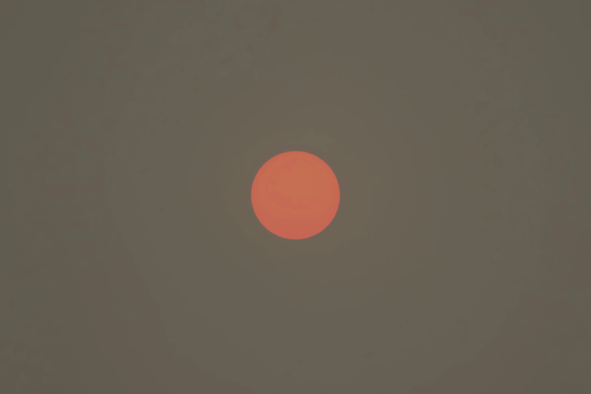 the sun shining orange through a smoke filled sky