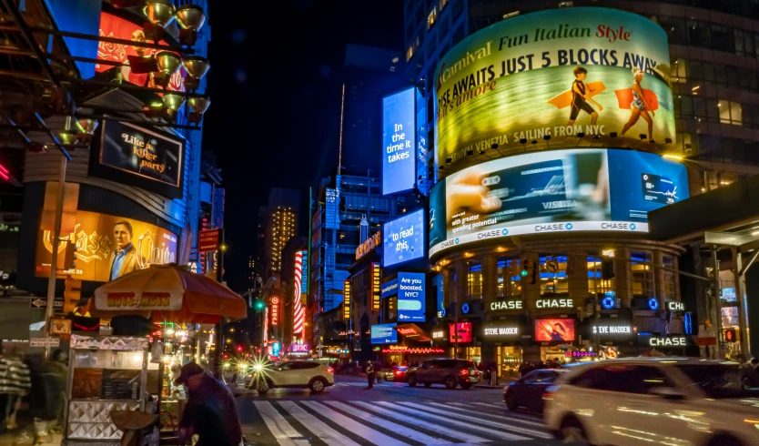 a street corner at night, with many pedestrians and taxis passing by