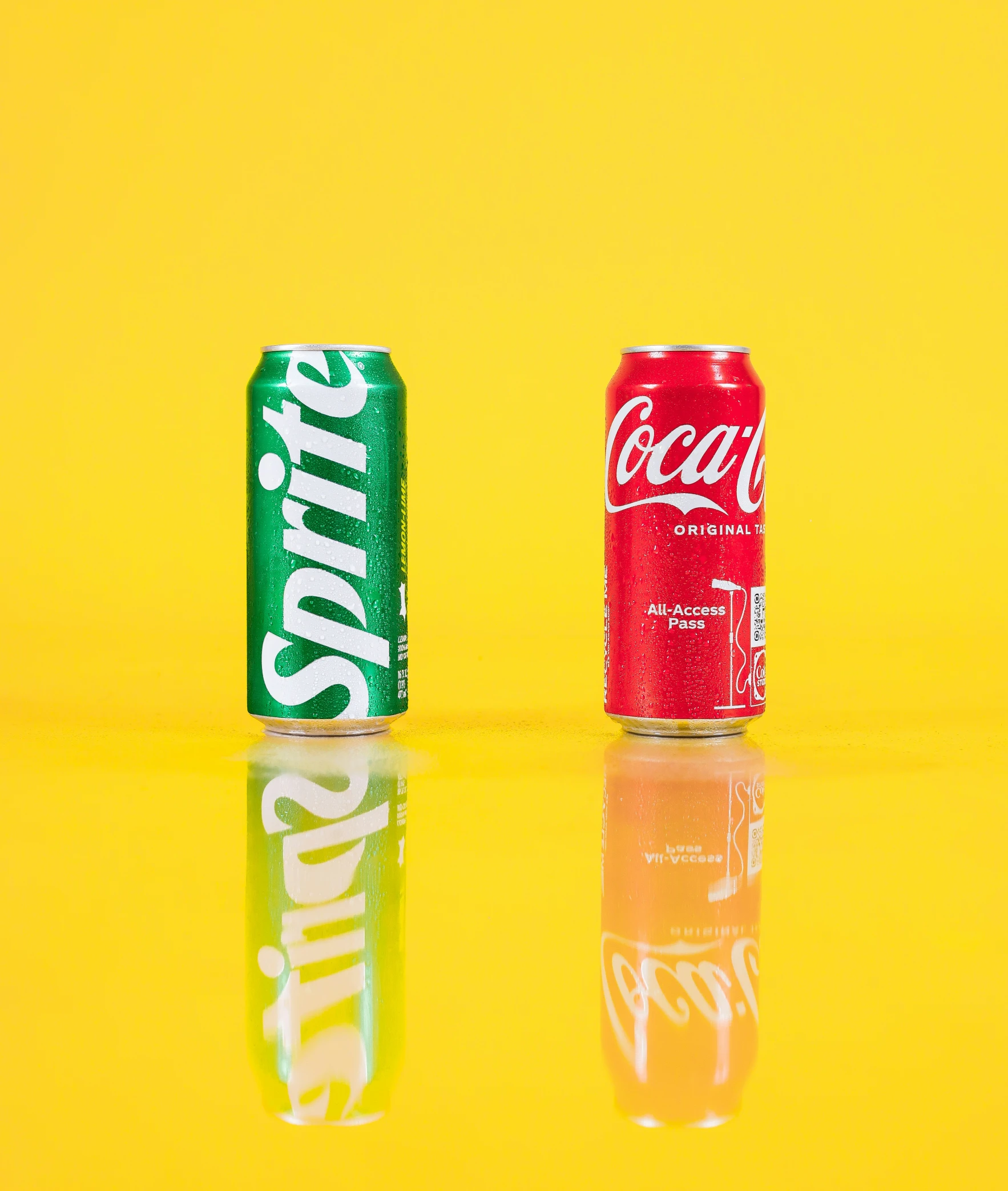 two sodas, one green and one red, are against a bright yellow background