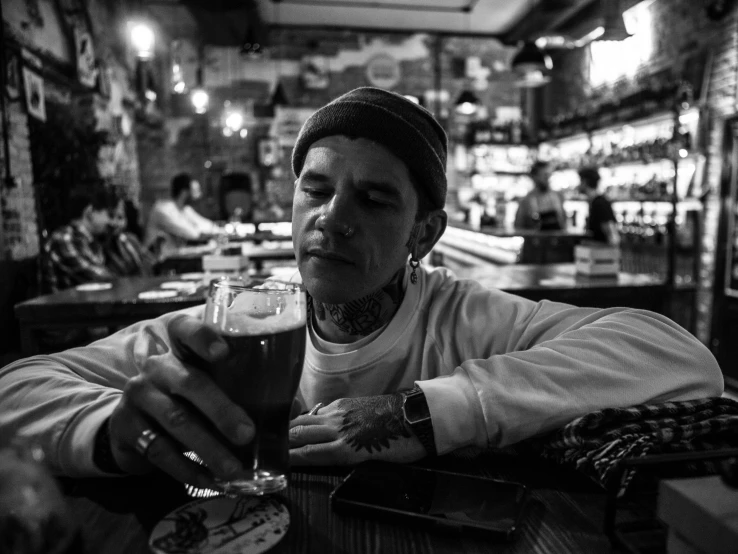 a man with a beard and tattoo, holding up a glass of beer