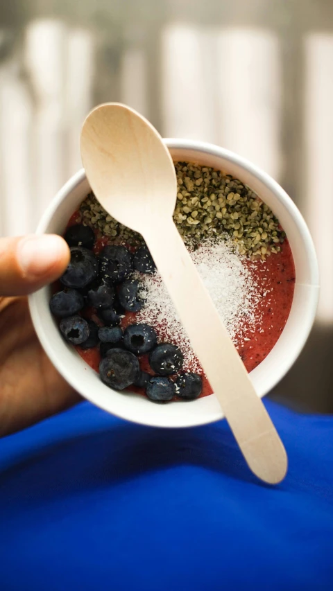 a hand is holding a plastic bowl full of blueberries and granola