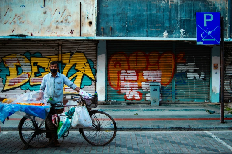 a man standing next to his bike in front of a building with graffiti