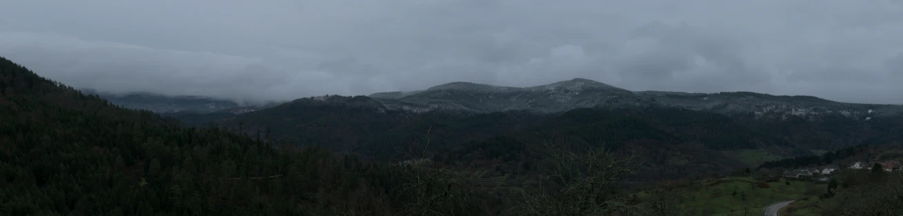 a mountain covered in trees under a cloudy sky