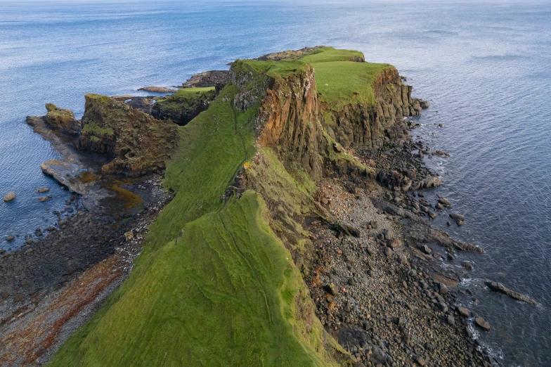 a cliff with grass at the edge of it next to the ocean