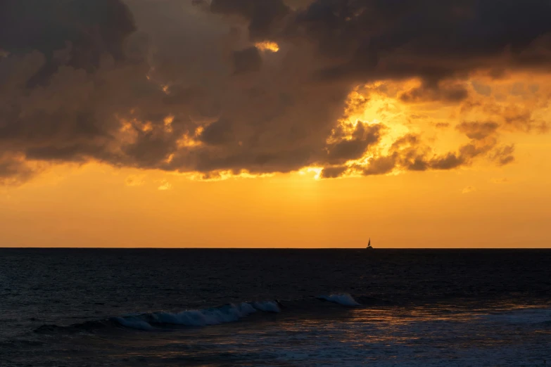 the sun shining through a stormy sky with a sailboat on the horizon