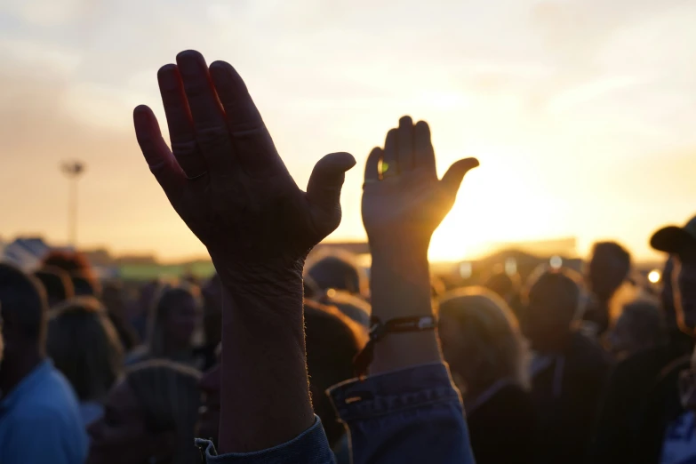 people raising their hands in the air as the sun sets