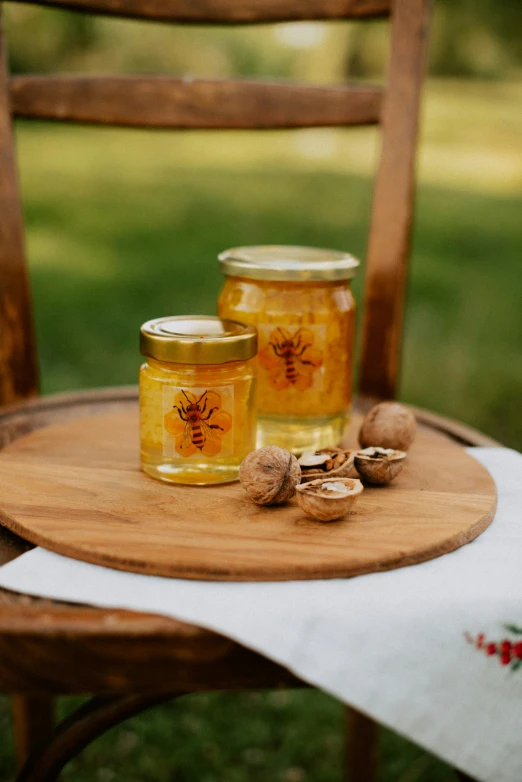 two jars of honey sitting on a wooden tray on top of a chair