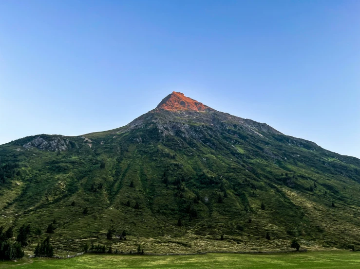 a mountain with a green field below and trees at the bottom