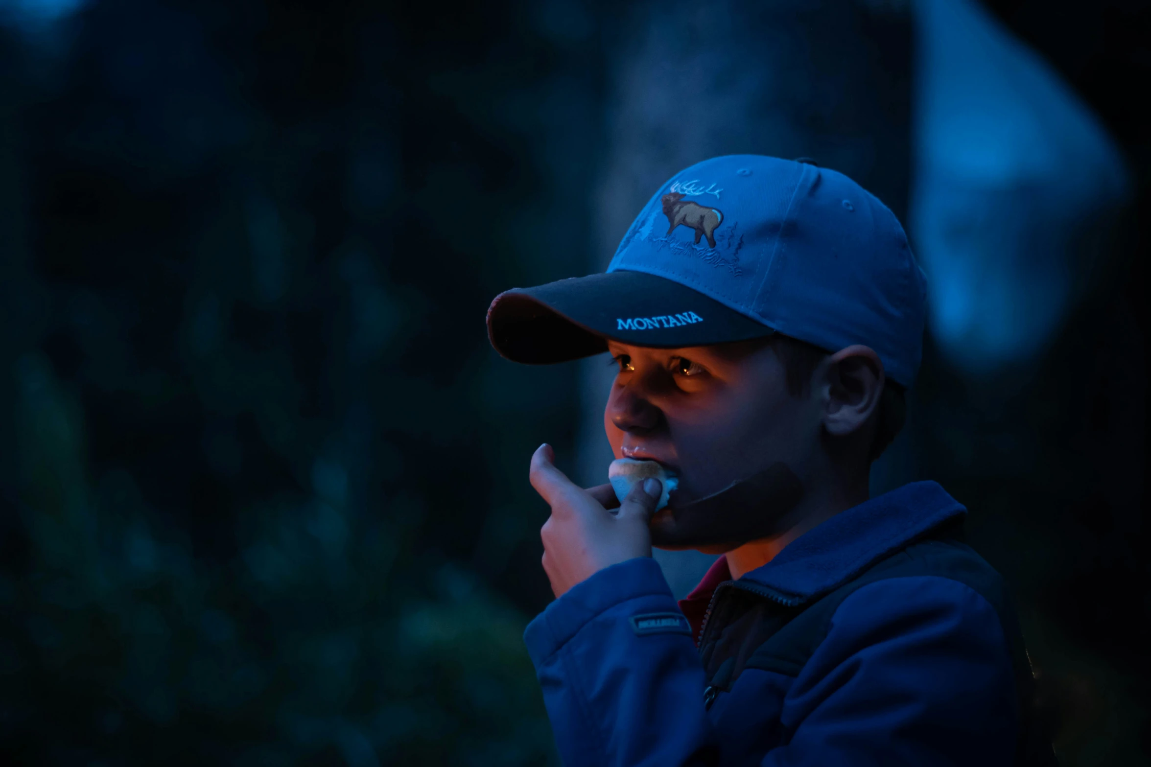 a little boy smoking soing at night while wearing a hat