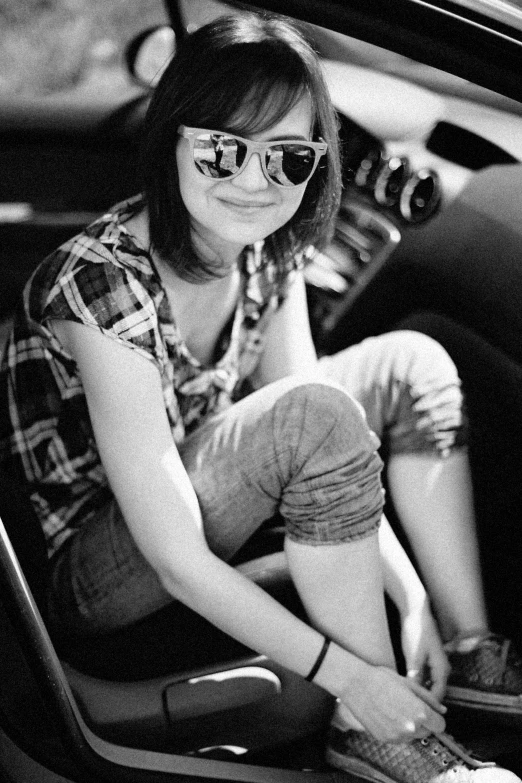 a woman in sunglasses and checkered shirt sitting in a car