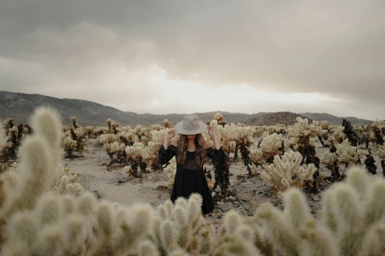 woman with hat in open desert field surrounded by cacti