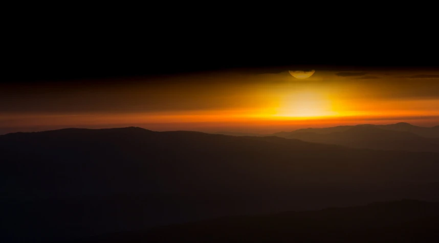 a view of some mountains at night and a bright sunset