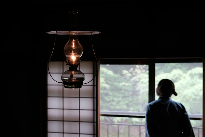 a person standing at a window looking outside with a lamp in the dark