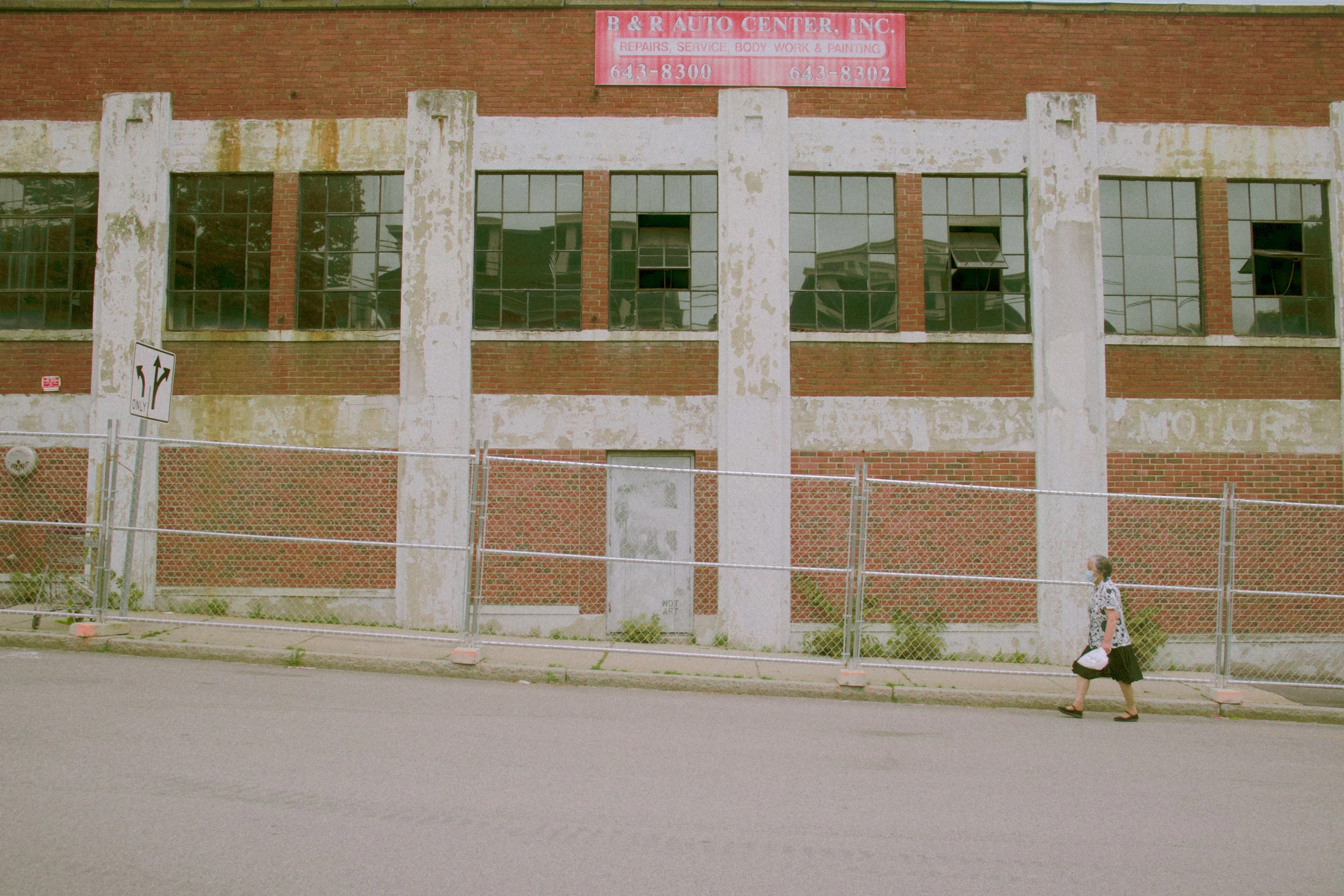 a person walks down the sidewalk by an abandoned building