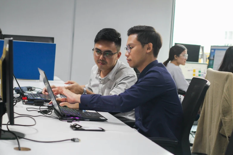 two men looking at laptop computers in an office