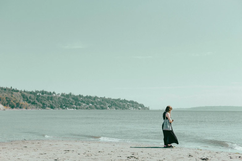 a woman standing on a beach, facing the ocean