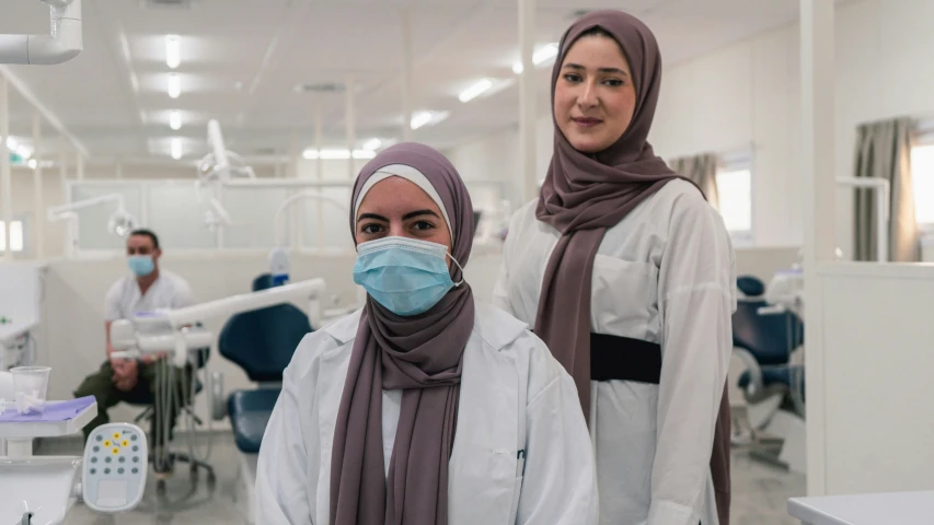 two women wearing scarves pose for a picture in an operating room