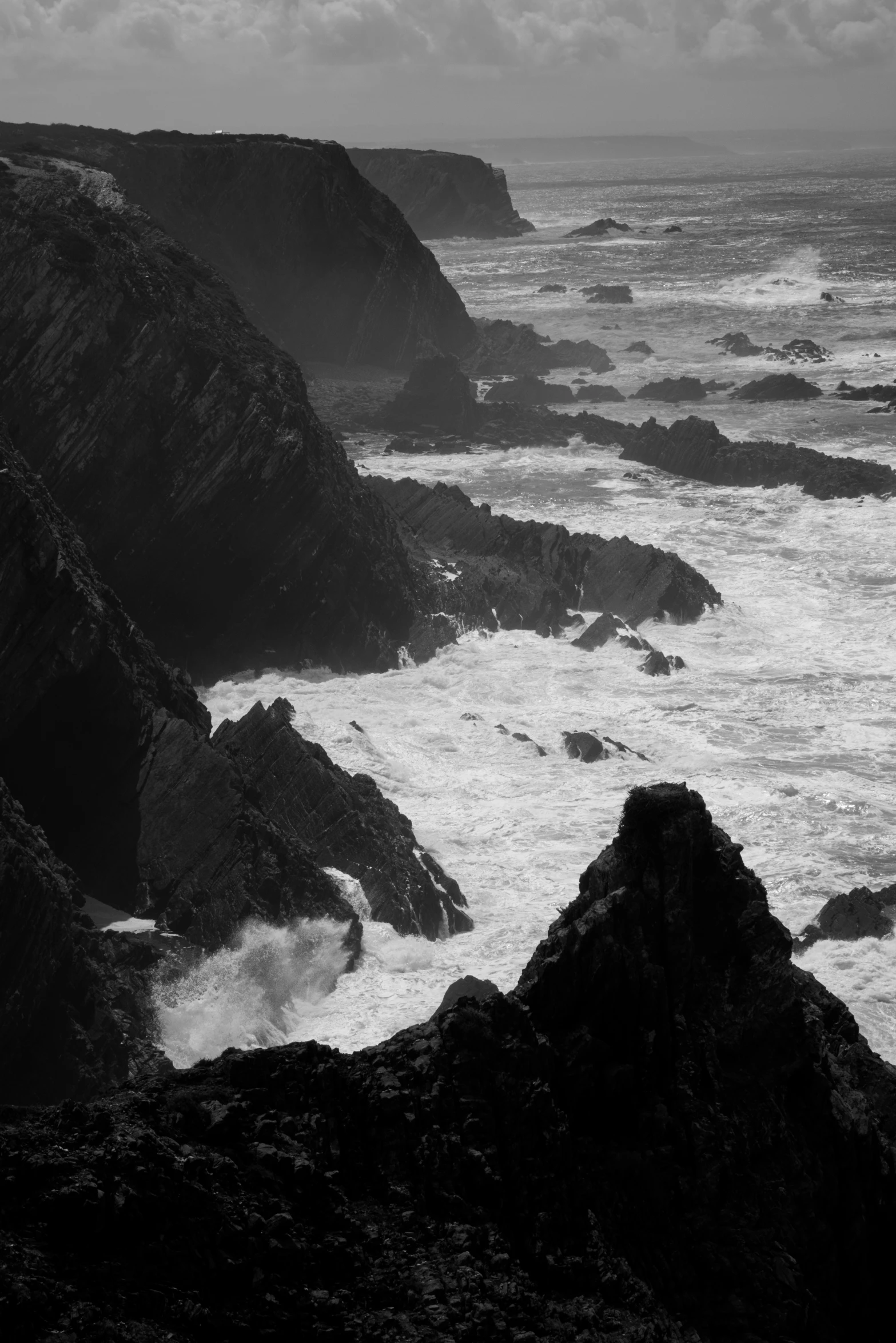 black and white image of rocky coastline with waves crashing into the shore