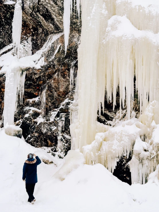 a man standing next to a snow covered waterfall in the woods