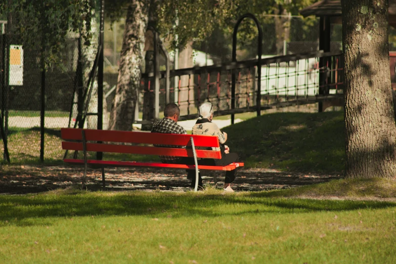 a man sitting on top of a red bench next to a tree