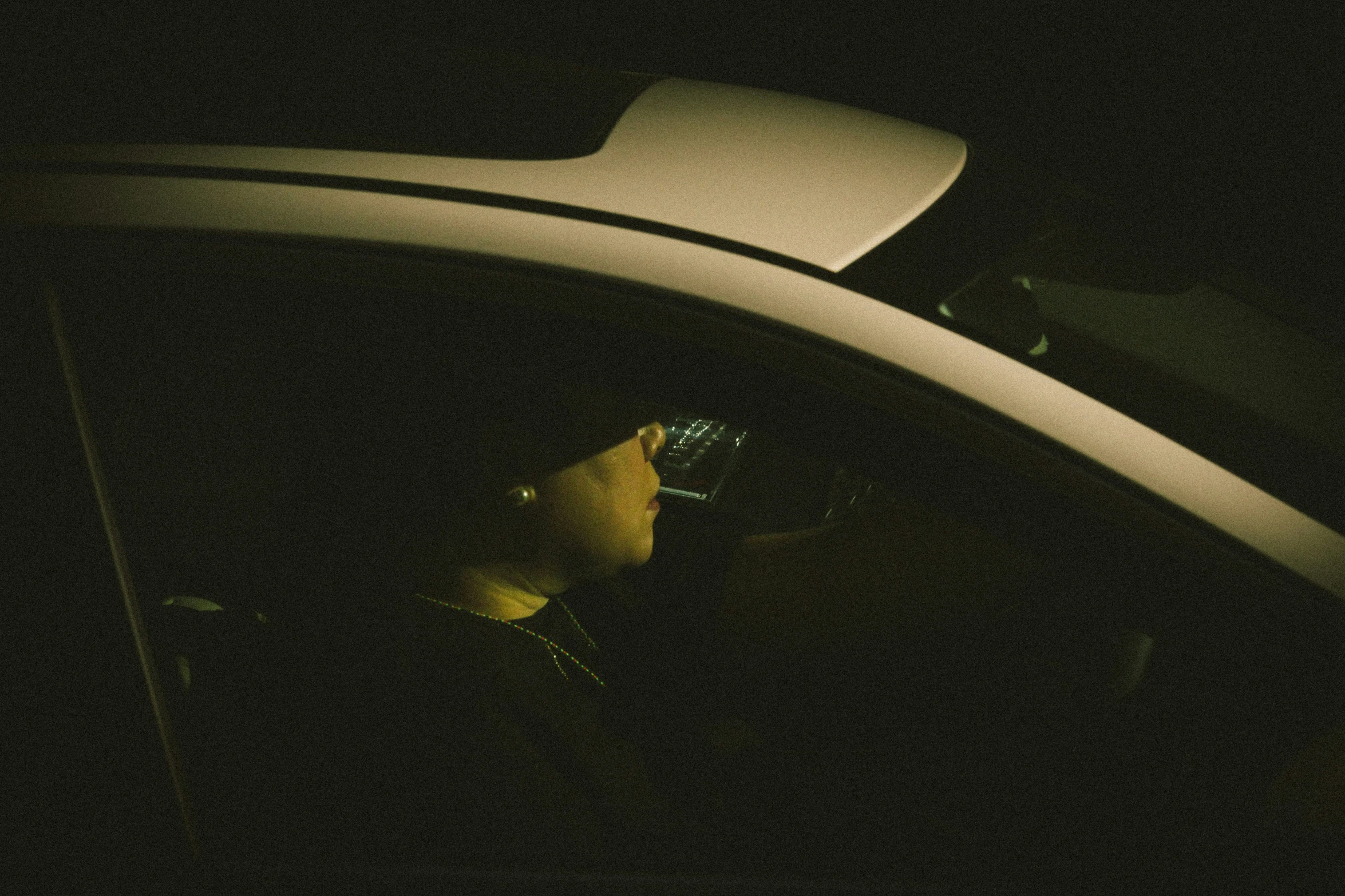 a man holding a cell phone standing in a car at night