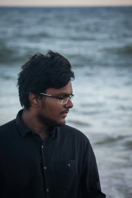 man with glasses standing by the water staring