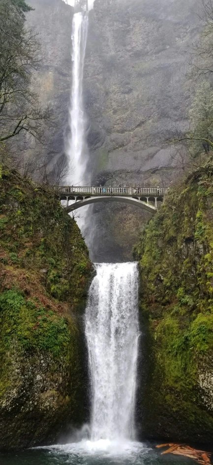 a waterfall with a bridge over it and a person walking across the falls