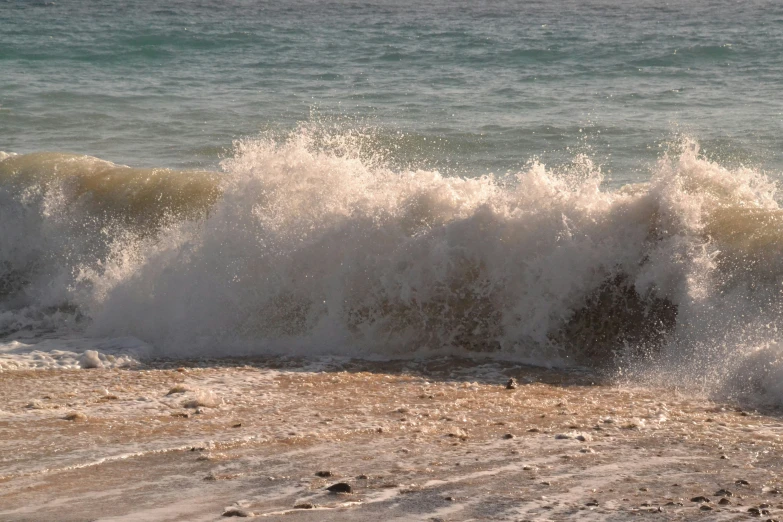 a wave breaking over a beach with the ocean in the background