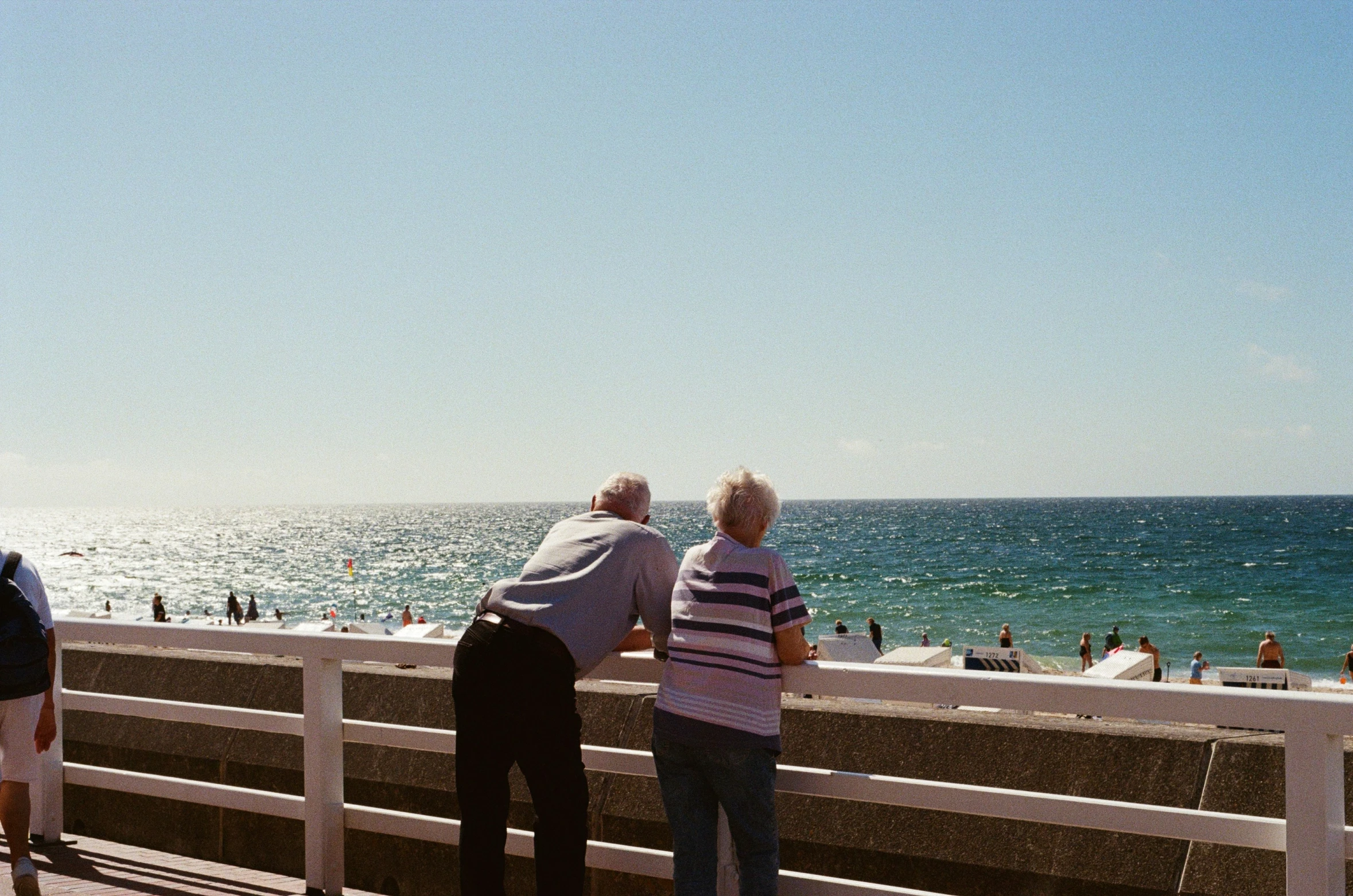 two men watching people on a pier near the ocean