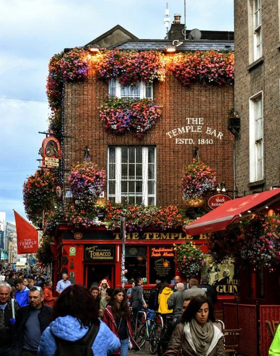 people walking on the street in front of a brick building with floral decorations hanging from it