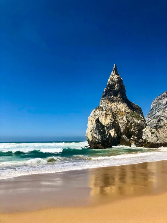 the rock in the ocean is sitting on a beach