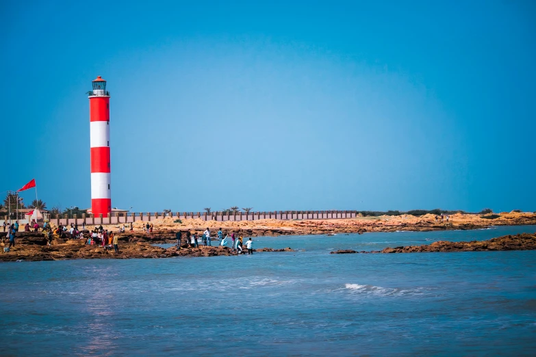 a red and white light house with people in the water near by