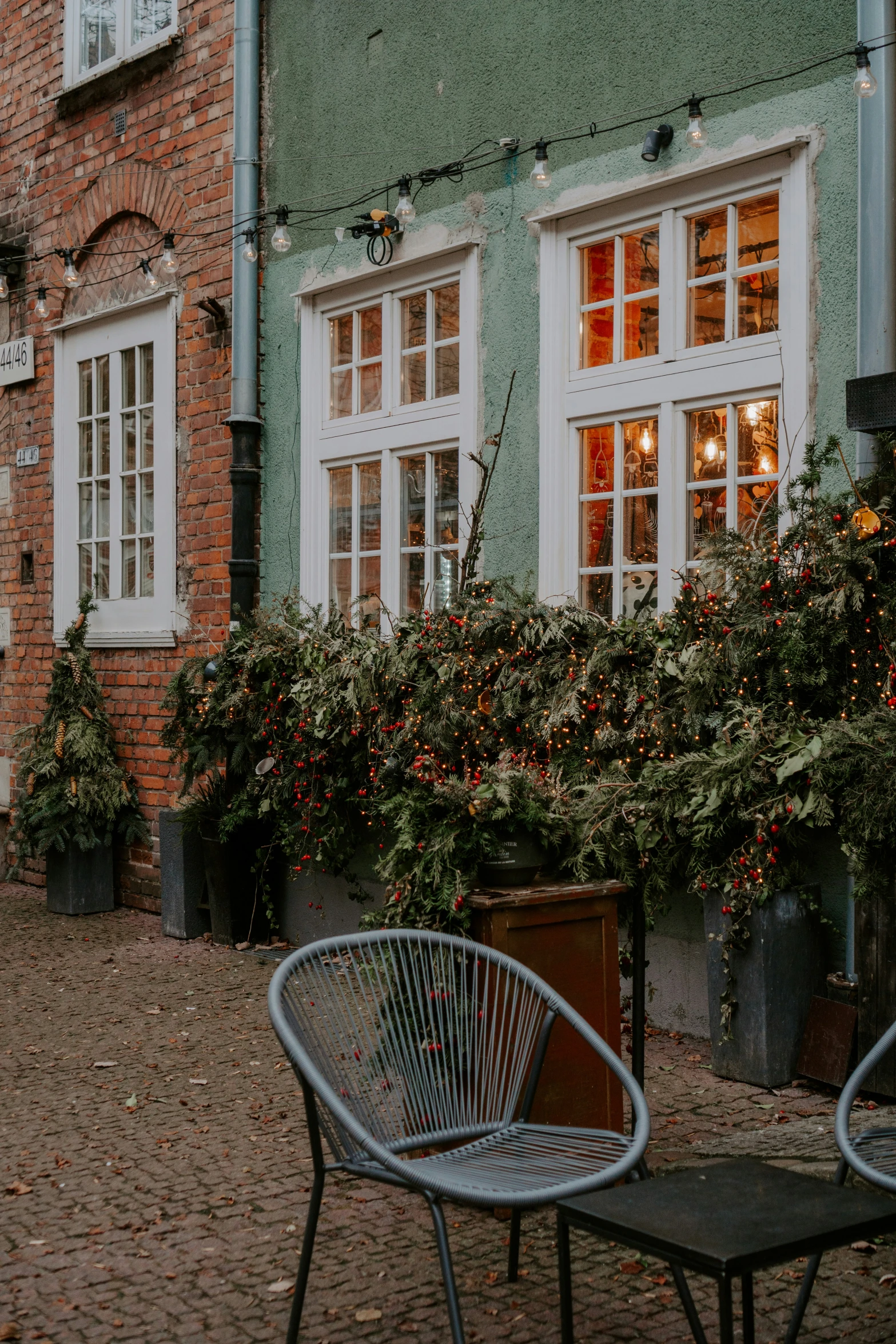 a green brick house with windows and plants surrounding it