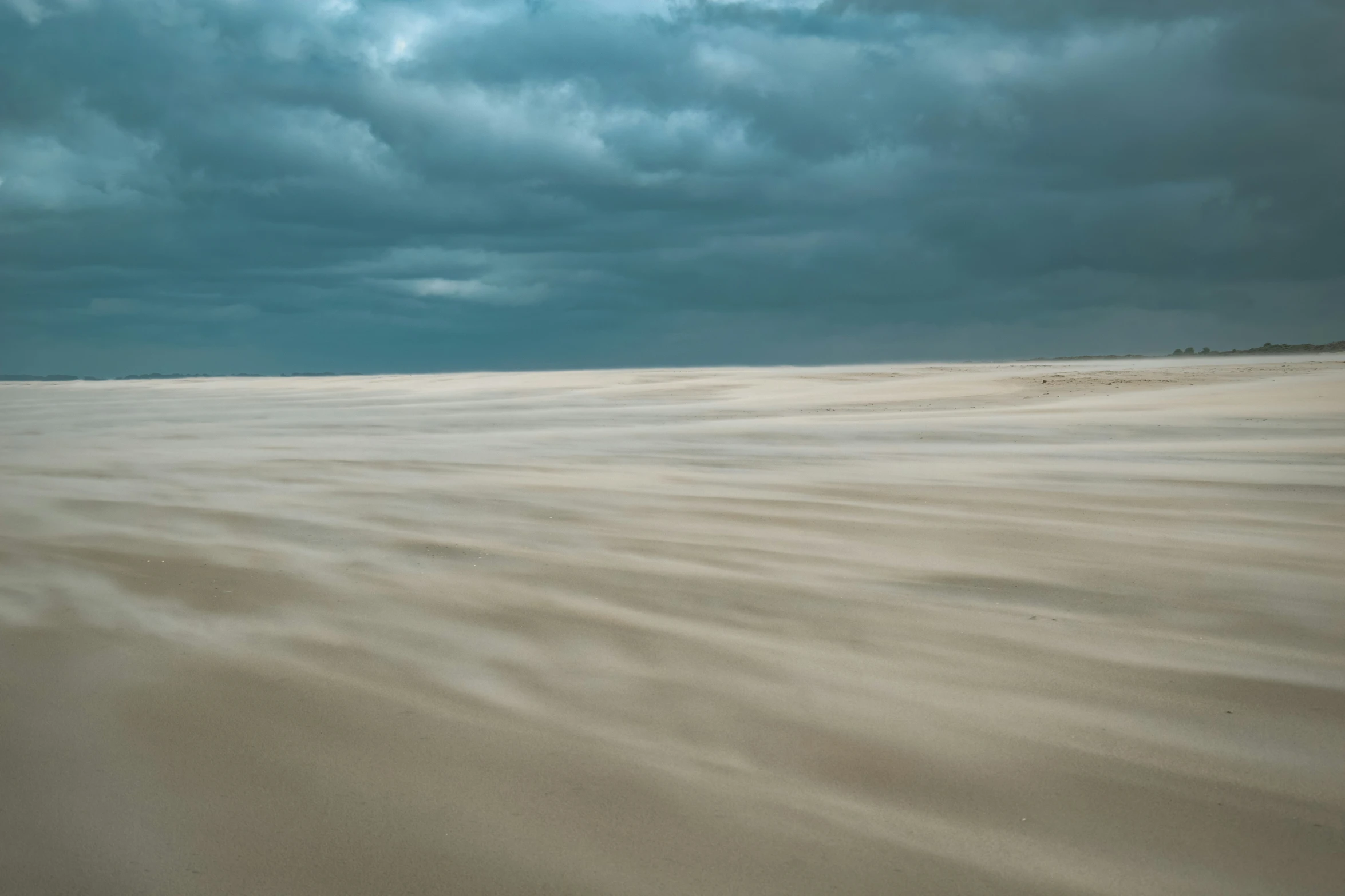 an empty beach with some dark clouds in the background