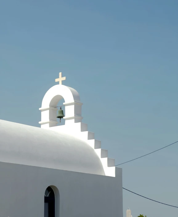 a white steeple with a cross and bell below