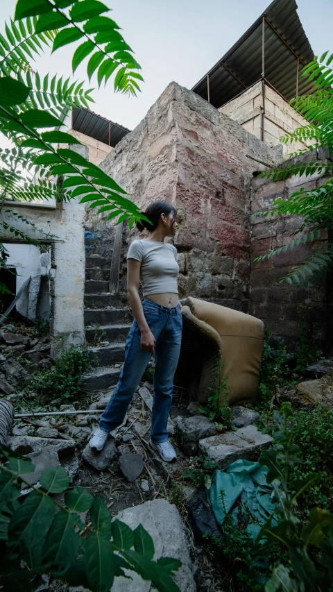 a young woman leaning against a chair on the steps in a overgrown area