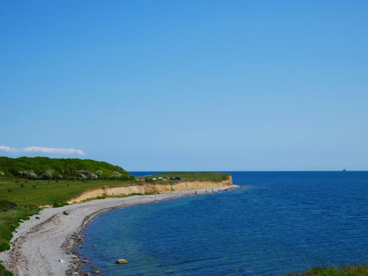 the rocky shore of an empty beach with green fields