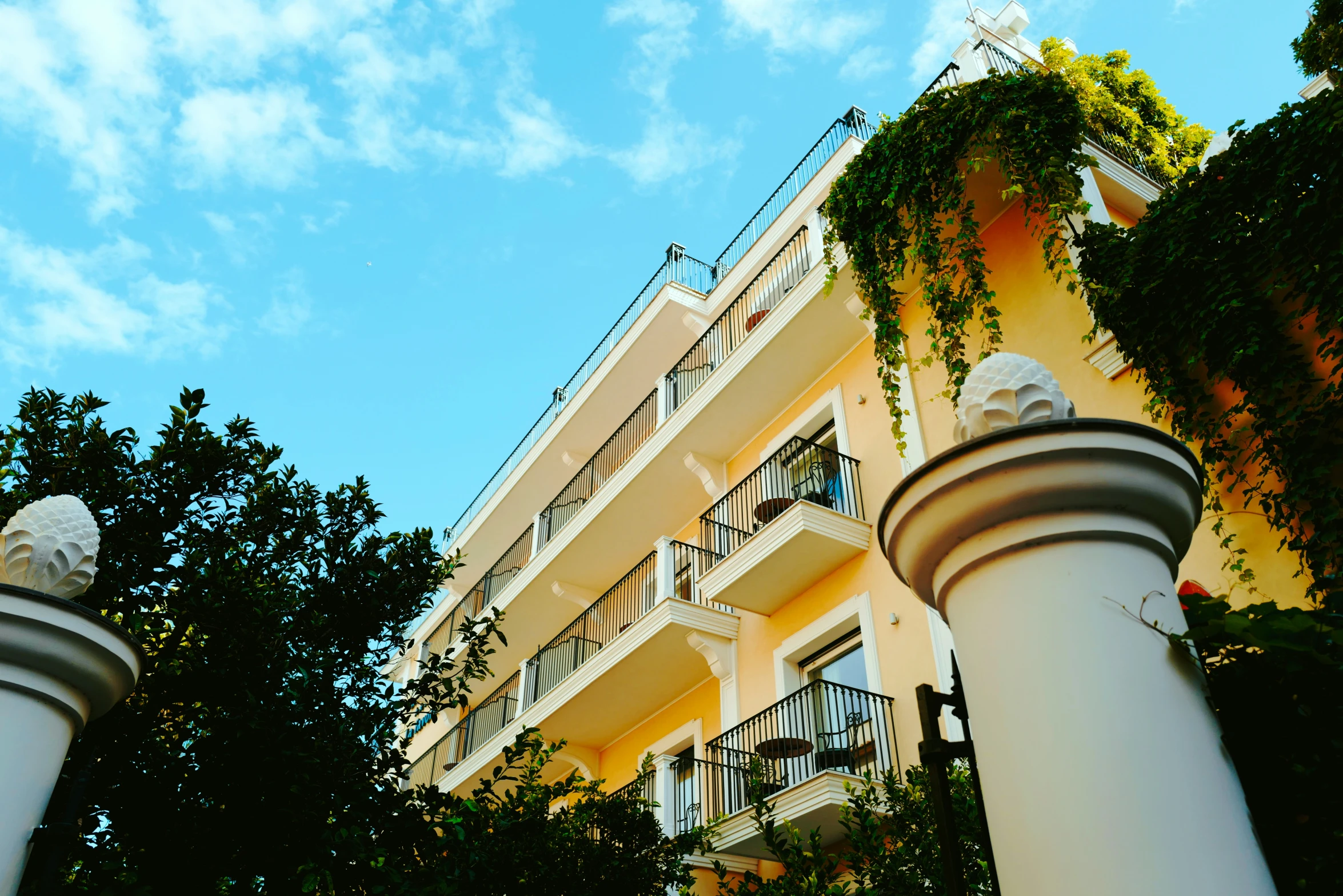 two statues on top of white columns in front of a yellow building