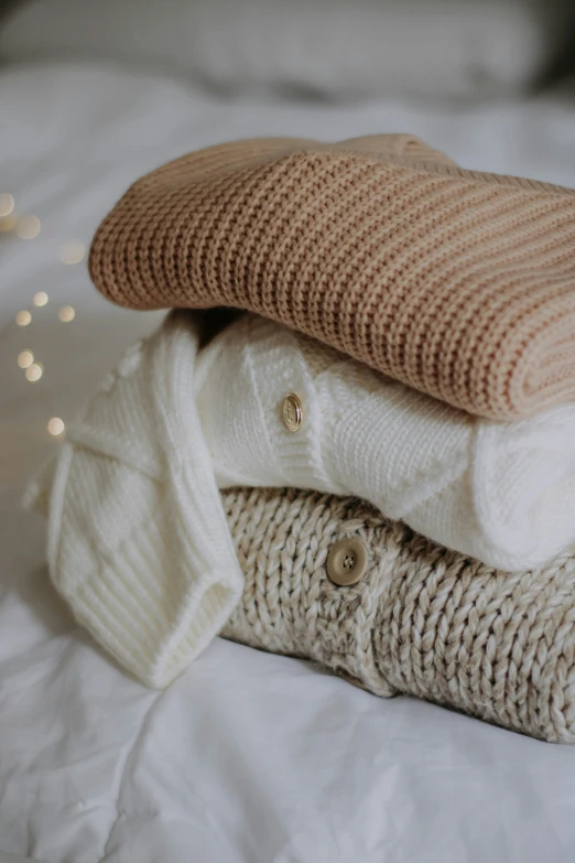 sweaters sit in a pile on a white bed sheet