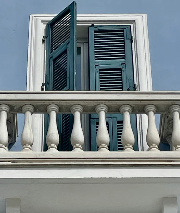 a balcony area that has a window with shutters on it