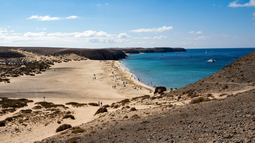 people walk along a sandy beach, near the ocean