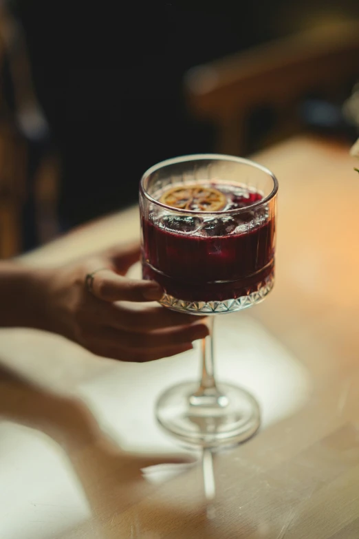 someone holding a wine glass with red liquid