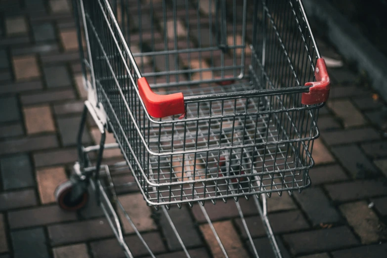 a shopping cart sits on brick pavement, with wheels