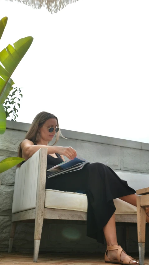 a woman sits on a sofa chair near some plants