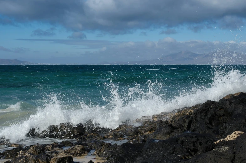 large waves crashing onto a rocky shore with blue sky