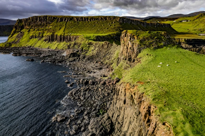 a lush green field sits above a cliff near the water